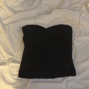 Svart tubtopp - Snygg svart tubtopp perfekt för en stilren look. Den är axelbandslös och har en tight passform som framhäver figuren. Passar utmärkt till både vardag och festliga tillfällen.