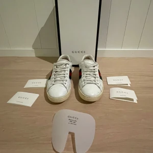 Vita sneakers från Gucci ace bee  - Säljer ett par vita Gucci sneakers med klassiska gröna och röda ränder samt en broderad guldfärgad bi-detalj på sidan. Skorna har snörning och är tillverkade i skinn. Perfekta för en stilren look. Priset kan vi diskutera, box o allt me på pulserna kommer med