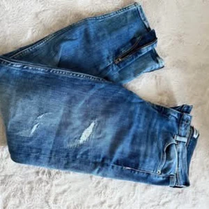 Blå jeans med slitningar - Snygga blå jeans med slitningar för en trendig look. Perfekta för en avslappnad stil. De har en klassisk femficksdesign och dragkedja.
