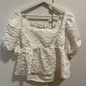 Vit blus med broderade detaljer - Charmig vit blus med puffiga kortärmar och vacker broderad design. Blusen har en fyrkantig halsringning och knytband i ryggen för en snygg touch.