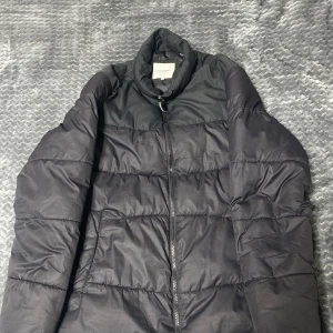 Svart pufferjacka från Jack & Jones - Säljer en svart pufferjacka från Jack & Jones i storlek M. Jackan har en dragkedja framtill och är perfekt för kyligare väder. Den har en stilren design med långa ärmar och en hög krage.