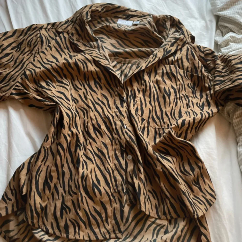 Snygg zebramönstrad skjorta med knappar och långa ärmar. Perfekt för att ge en djärv touch till din outfit.. Paidat.