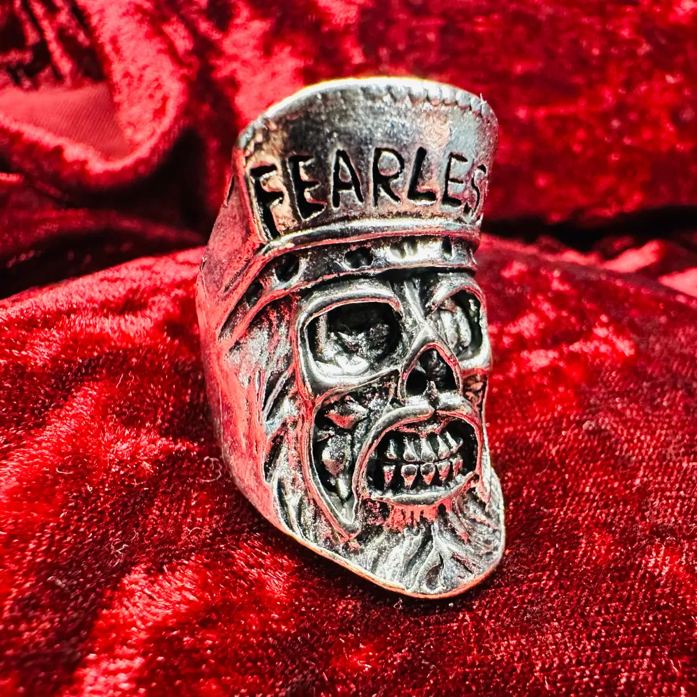 Unik och tuff ring i silverfärg med en detaljerad dödskalle och texten 'Fearless' ingraverad. Perfekt för att ge en edgy touch till din stil. Ringen har en robust design och är ett statement-smycke för den modige. Höjd cirka 3,5, innerdiameter 2,1 cm men öppen bak så justerbar storlek. Ny och oanvänd. . Asusteet.