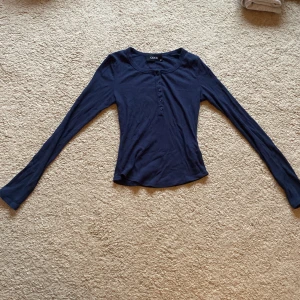 Marinblå ribbad tröja från Cider - Säljer en stilren marinblå tröja från Cider i ribbat material. Tröjan har långa ärmar och knappar framtill som ger en snygg detalj. Perfekt för en avslappnad look.