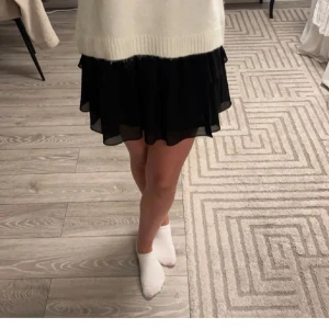 Svart kjol från Chelsea - Snygg svart kjol från Chelsea med volangdetaljer. Kjolen har en elastisk midja för bekväm passform och är perfekt för att ge en stilfull look.