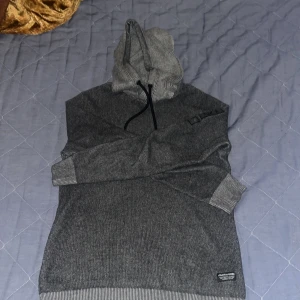 Grå hoodie från Jack & Jones - Säljer en stilren grå hoodie från Jack & Jones. Den har en justerbar huva med svarta snören och ribbade muddar vid ärmslut och nederkant. Perfekt för en avslappnad look. Skick är 8/10.