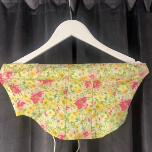 Blommig korsett från NLY One - Säljer en färgglad blommig korsett från NLY One i storlek M. Den har ett vackert mönster i rosa, gult och grönt med snörning bak för justerbar passform. Perfekt för att liva upp garderoben!