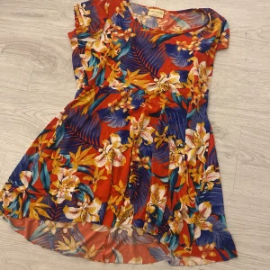 Blommig klänning från Bobbie Brooks - Säljer en färgglad klänning från Bobbie Brooks med ett tropiskt blommönster i rött, blått och gult. Klänningen har korta ärmar och en luftig passform, perfekt för varma dagar. Tillverkad i Egypten.