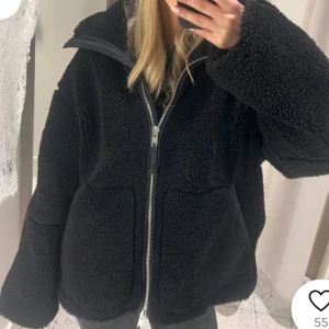 Svart teddyjacka med dragkedja - Mysig svart teddyjacka med dragkedja framtill. Perfekt för kyliga dagar med sin fluffiga och varma design. 