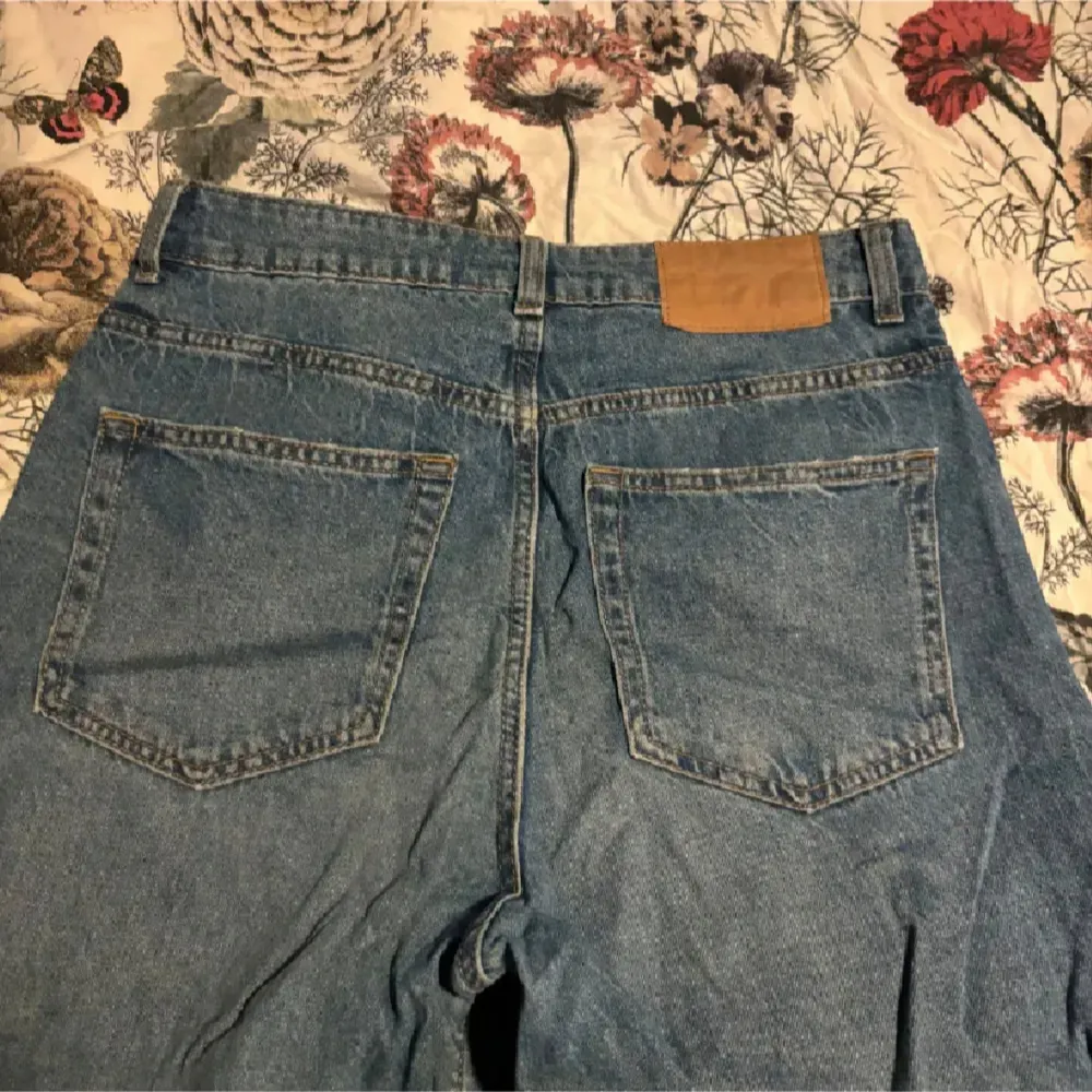 Säljer ett par klassiska blå jeans med hög midja och breda ben. De har en traditionell femficksdesign och stängs med dragkedja och knapp. Perfekta för en avslappnad stil.. Farkut & Housut.