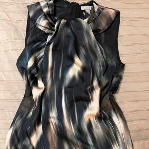 Mönstrad ärmlös festtopp  - Snygg ärmlös topp med abstrakt mönster i mörka och ljusa toner. Klänningen har en elegant drapering framtill och en diskret dragkedja i ryggen. Perfekt för en stilfull look. Strl Cs men passar mig som har S