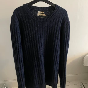 Mörkblå ribbad tröja från East West - Säljer en stilren mörkblå ribbad tröja från East West. Tröjan har en klassisk rund hals och långa ärmar, perfekt för kyligare dagar. Den är både bekväm och snygg, ett måste i garderoben!