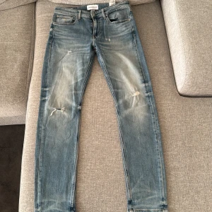 Blå jeans från Calvin Klein - Snygga blå jeans från Calvin Klein med slitna detaljer och en klassisk femficksdesign. De har en dragkedja och knapp framtill samt märkets logga på bakfickan och insidan. Perfekta för en avslappnad stil.