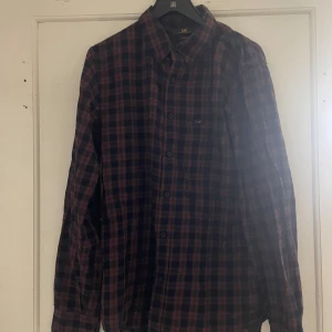 Rutig skjorta från Lee - Säljer en rutig skjorta från Lee i mörka nyanser av blått och rött. Skjortan har långa ärmar och knappar framtill. Perfekt för en avslappnad stil.