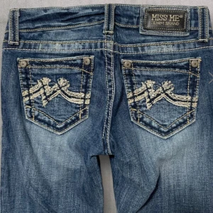 Blå jeans med broderade detaljer från Miss Me - Snygga blå jeans från Miss Me med unika broderade detaljer på bakfickorna. De har en lågmidjad passform och en bootcut-stil som ger en klassisk look. Perfekta för dig som vill ha något extra i garderoben!