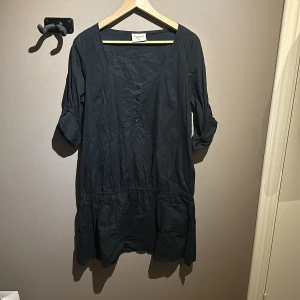 Svart klänning från Gina Tricot - Snygg svart klänning från Gina Tricot i bomull. Den har trekvartsärmar med knappdetalj och en v-ringad hals. Perfekt för en stilren look.