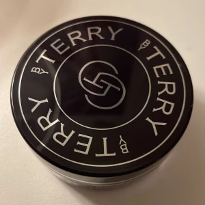 By Terry Hyaluronic Hydra-Powder - Endast provad en gång    Nypris 559 kr. .Säljer ett By Terry Hyaluronic Hydra-Powder. Detta transparenta puder är perfekt för att sätta smink och ge en matt finish. Innehåller hyaluronsyra för extra återfuktning. Kommer i en rund burk med svart lock och vit text.