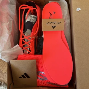 Adidas F50 Elite SG Fotbollsskor - Säljer ett par Adidas F50 Elite SG fotbollsskor i en iögonfallande röd färg med svarta detaljer. Skorna har snörning och är designade för optimal prestanda på fotbollsplanen. Perfekta för spel på mjuka underlag.