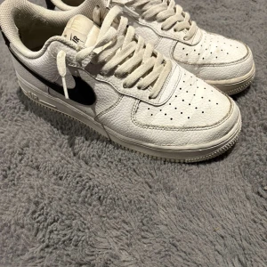 Nike Air Force 1  - Säljer ett par klassiska Nike Air Force 1 sneakers i vitt med svart swoosh. Skorna har snörning och är tillverkade i skinn med perforerade detaljer för extra ventilation. Perfekta för en stilren look. Med kärlek kan man få dessa att se nya ut igen 