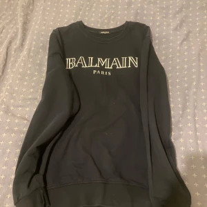 Svart sweatshirt från Balmain - Snygg svart sweatshirt från Balmain med vit logotyp på bröstet. Tröjan har långa ärmar och en klassisk rund halsringning. Perfekt för en stilren och avslappnad look.