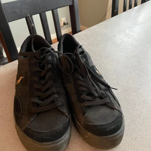 Svarta sneakers från Ralph Lauren - Snygga svarta sneakers från Ralph Lauren med klassisk design och snörning. Skorna har en diskret logga på sidan och är tillverkade i mocka och syntetmaterial.