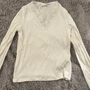 Säljer en stilren vit långärmad topp från Gina Tricot med v-ringad spetsdetalj. Perfekt för en elegant och bekväm look. Passar bra till både jeans och kjol. 🌟