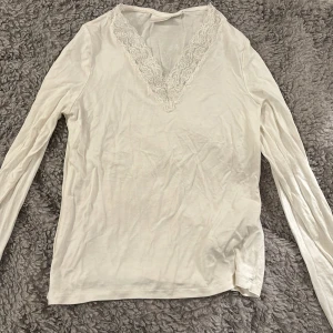 Vit långärmad topp från Gina Tricot - Säljer en stilren vit långärmad topp från Gina Tricot med v-ringad spetsdetalj. Perfekt för en elegant och bekväm look. Passar bra till både jeans och kjol. 🌟