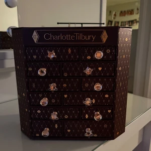Sminkkalender från Charlotte Tilbury - Lyxig sminkkalender från Charlotte Tilbury med flera lådor för förvaring av sminkprodukter. Perfekt för att organisera och förvara dina favoritprodukter. Elegant design med dekorativa handtag och mönster.