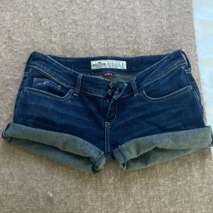 Mörkblå jeansshorts från Hollister - Snygga mörkblå jeansshorts från Hollister med uppvikta ben och klassisk femficksdesign. Perfekta för en avslappnad sommarlook. Stretchmaterial för extra komfort. Lågmidjade 