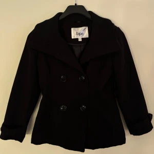 Svart kappa från Bonprix Collection - Snygg svart kappa från Bonprix Collection med dubbelknäppning och bred krage. Perfekt för kyligare dagar med sin stilrena design och långa ärmar. En klassisk jacka som passar till många tillfällen.