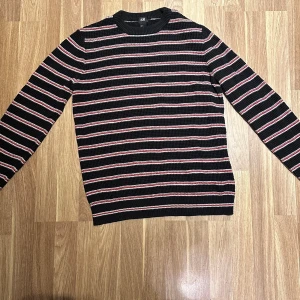 Svart och röd randig tröja  - Snygg svart tröja med röda och vita ränder från H&M i storlek M. Perfekt för en avslappnad stil. Tröjan har långa ärmar och en rund halsringning och är perfekt till vinter och höst. Oanvänd! 