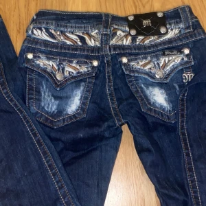 Blå jeans med broderade detaljer från Miss Me - Snygga blå jeans från Miss Me med unika broderade detaljer. Jeansen har en klassisk femficksdesign och en lågmidjad passform. Dom är också i parfekt skick 
