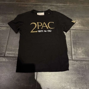 Svart T-shirt med 2PAC från Replay - Snygg svart T-shirt från Replay med guldtryck av '2PAC 1971 to ∞' på framsidan och 'ALL EYEZ ON ME' på baksidan. Den är en del av en limited edition-kollektion.