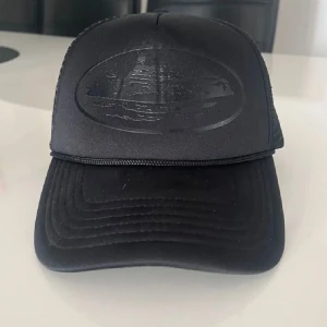 Svart corteiz  keps - Snygg svart keps med broderad logga framtill och meshpaneler på sidorna för extra ventilation. Perfekt för en avslappnad stil. 