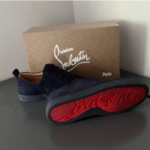 Christian Louboutin sneakers med röd sula - Snygga Christian Louboutin sneakers i mörkblå mocka med den ikoniska röda sulan. Skorna har en elegant design med snörning och kommer i originalförpackning med dustbag.