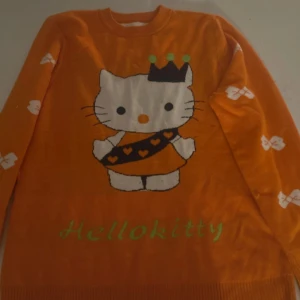 Orange Hello Kitty tröja - Säljer en söt orange tröja med Hello Kitty-motiv och vita rosetter. Tröjan har långa ärmar och är perfekt för den som älskar färgglada och lekfulla plagg.