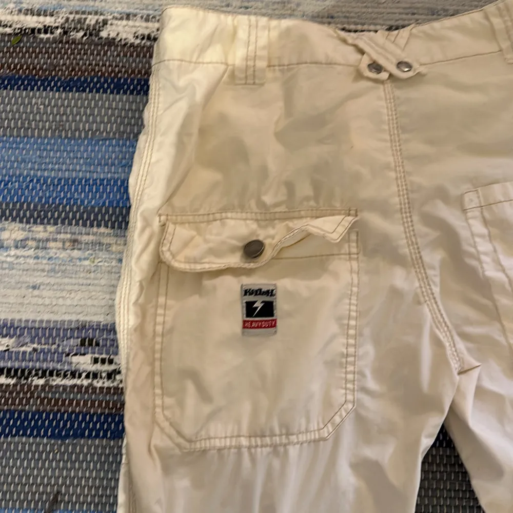 Säljer ett par beige cargopants från Killah med flera praktiska fickor och snörning vid bensluten. Byxorna har en knapp och dragkedja framtill för enkel stängning. Perfekta för en avslappnad stil. Byxa från -90talet. Fint skick! . Farkut & Housut.