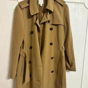 Beige trenchcoat med knappar - Snygg beige trenchcoat med klassisk design och svarta knappar. Jackan har ett bälte i midjan. Den är knappt använd. Perfekt för höst och vår. Skriv privat för mer bilder 