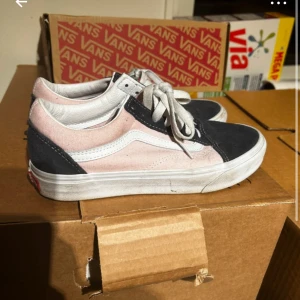 Vans sneakers i rosa och svart - Snygga Vans sneakers med en kombination av rosa och svart mocka. Skorna har den klassiska vita vågiga linjen på sidan och vita snören. Perfekta för en avslappnad stil.