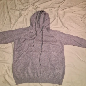 Grå hoodie - Säljer en helt ny stilren grå hoodie med långa ärmar och justerbar huva. Perfekt för en avslappnad look. Ribbstickade muddar vid ärmslut och nederkant ger en skön passform.
