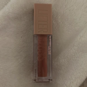 Läppglans från Maybelline - Snyggt läppglans från Maybelline med en lyxig förpackning. Färgen är en naturlig nude-ton som ger en fin glans och volym till läpparna. Perfekt för en fräsch look. Den är helt oanvänd 
