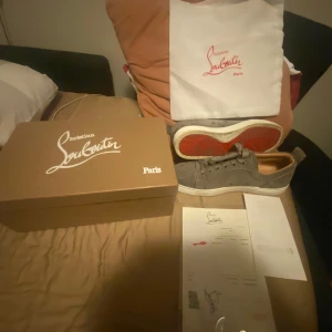 Grå sneakers från Christian Louboutin - Snygga grå sneakers från Christian Louboutin med klassisk röd sula. Skorna har snörning och är perfekta för en stilren look. Storlek 42 inga skador🔥