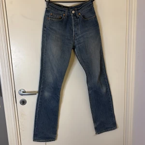 Levi's 501 jeans - Klassiska blå Levi's 501 jeans med knappgylf och femficksdesign. Dessa jeans har en straight passform och är tillverkade i slitstarkt denim. Perfekta för en tidlös stil.