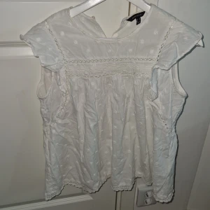 Vit blus från Cortefiel - Säljer en söt vit blus från Cortefiel med prickigt mönster och spetsdetaljer. Blusen är ärmlös och har en luftig passform, perfekt för varma dagar. Den har fina volanger vid ärmhålen och en rund halsringning. Passar mig som har stl S/Xs 