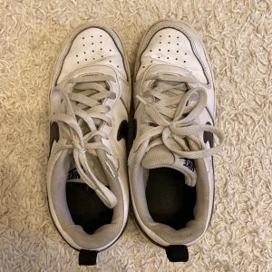 Vita Nike sneakers med svart swoosh - Snygga vita Nike sneakers med svart swoosh och snörning. Perfekta för en avslappnad stil. Skorna har en klassisk design med en bekväm sula.