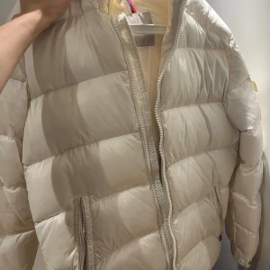 Vit dunjacka från Moncler - Säljer en stilren vit dunjacka från Moncler med dragkedja och praktiska fickor. Skador på jackan syns i bilden. Acceptabel skick. 
