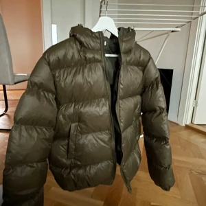 Olivgrön dunjacka med huva - Oanvänd, Säljer en olivgrön dunjacka med huva och dragkedja. Jackan är perfekt för kyligare väder och har en pufferdesign som ger extra värme. Den är liten i storleken, sitter som en S ☺️