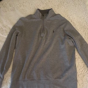 Grå tröja med dragkedja från Ralph Lauren - Snygg grå tröja från Ralph Lauren med halv dragkedja och broderad logga på bröstet. Nypris omkring 2000 kronor. Den är använd max 2 gånger alltså i helt nytt skick! Rätt liten i storlek så passar M fast den är storlek L.