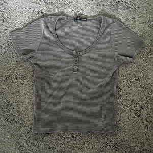 Brandy Melville topp - Säljer en grå randig topp från Brandy Melville med korta ärmar och knappar framtill💗🫶🏼