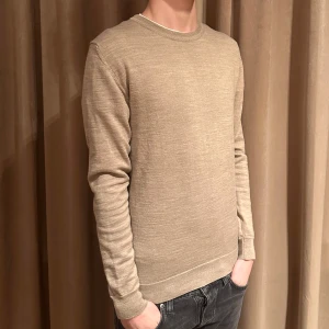 Stickad tröja - Tja, säljer denna stickade tröja i en väldigt snygg beige färg med en blandning av 50% ny ull och 50% akryl. Tröjan är i väldigt fint skick utan defekter. Modellen på bilden är 183. Hör av dig vid funderingar.